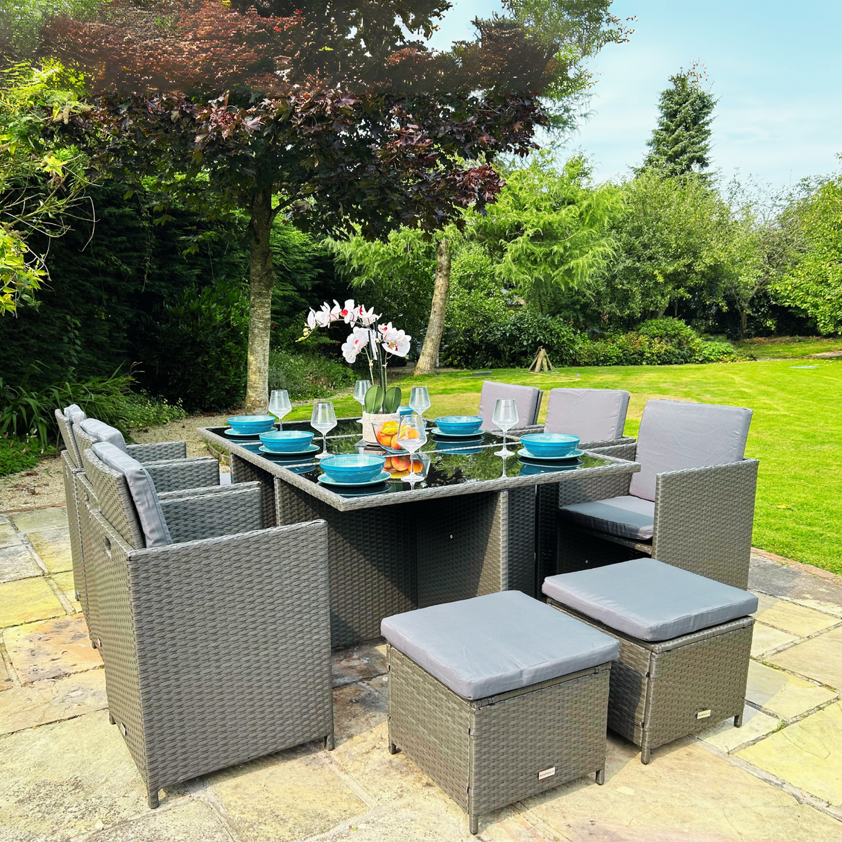 Outdoor patio set with table and chairs on a paved area with greenery in the background
