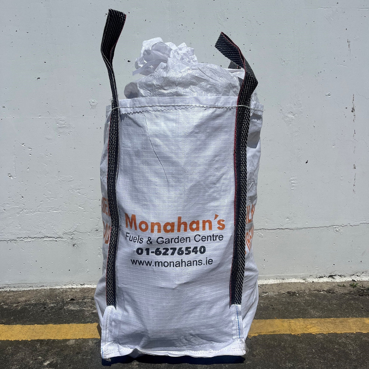 White bulk bag with black text and branding against a gray wall.