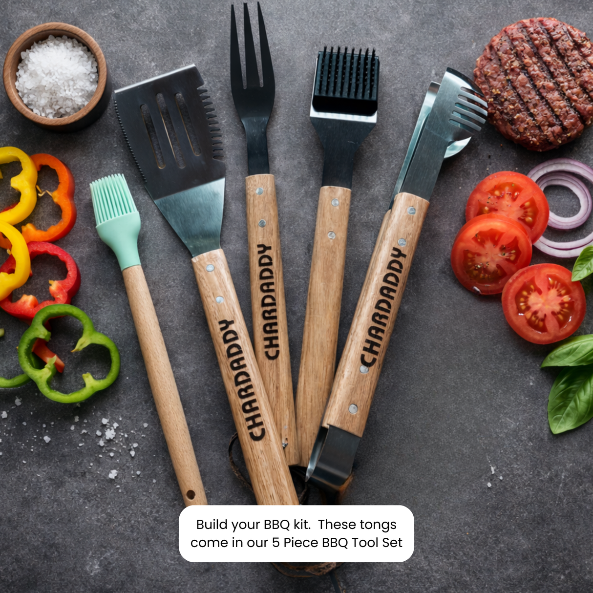 Set of barbecue tools with 'CHARDADDY' branding on a dark surface with vegetables.