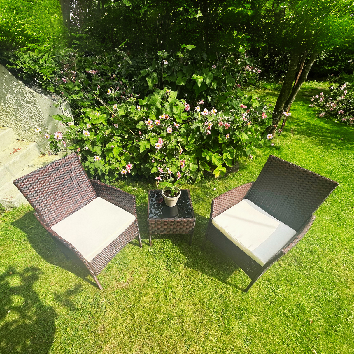 Two wicker chairs with cushions on a grassy area with flowers and plants.