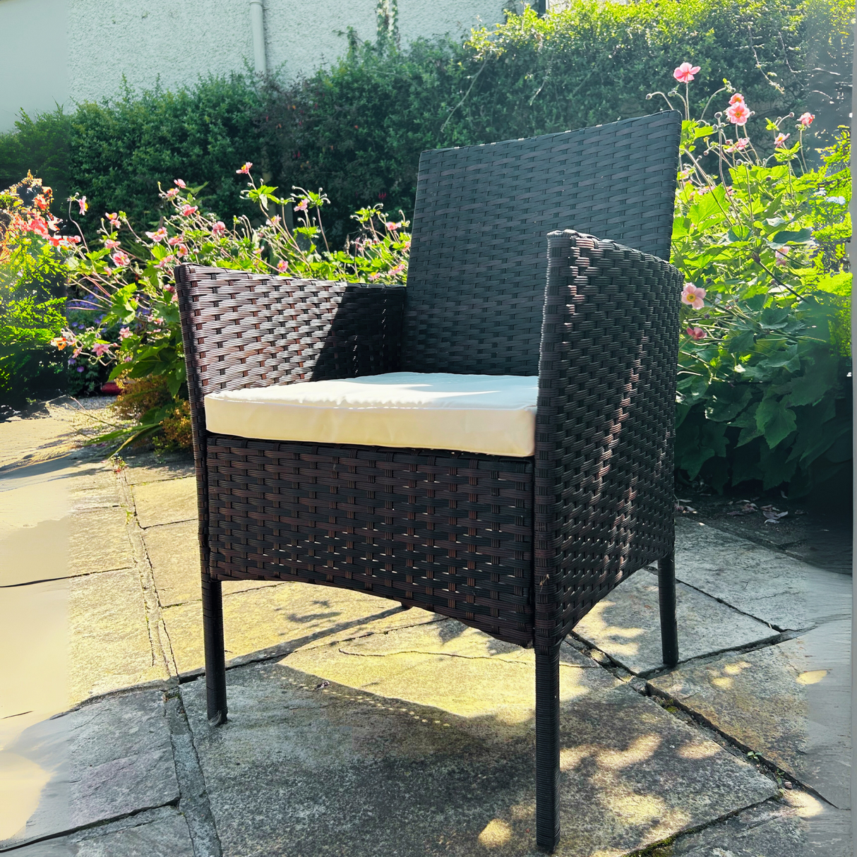 Wicker chair with a cushion on a stone patio with flowers and plants in the background