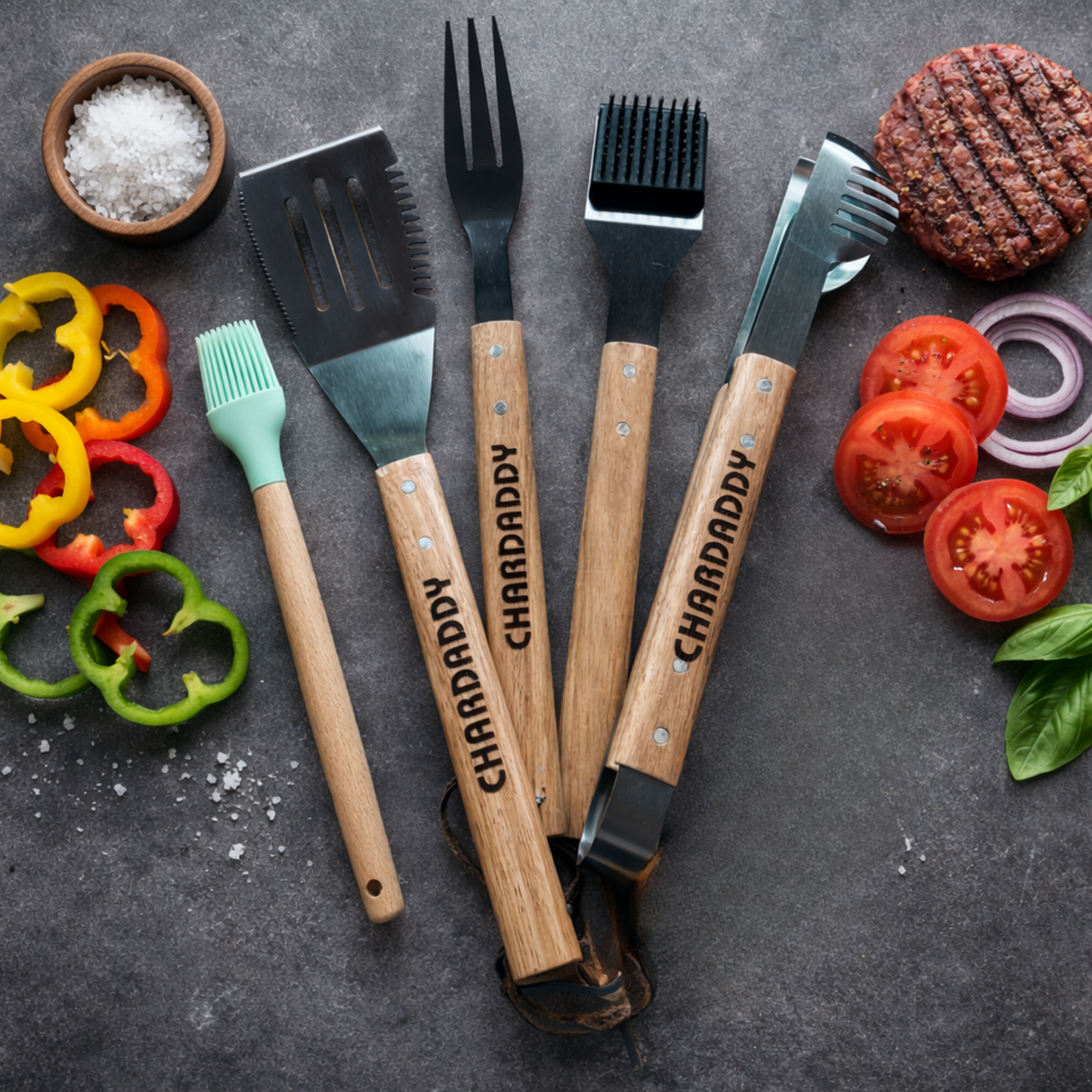 Barbecue tools with 'CHARDADDY' branding on a dark surface with grill ingredients.