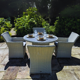 Outdoor patio set with a round table and four chairs on a stone patio.