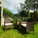 Two wicker chairs with cushions on a grassy lawn with a garden background