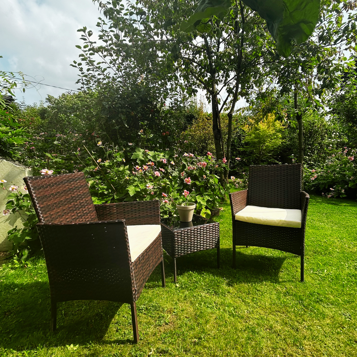 Garden setting with wicker furniture on a grassy area with flowers and trees in the background.