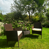 Garden setting with wicker furniture on a grassy area with flowers and trees in the background.